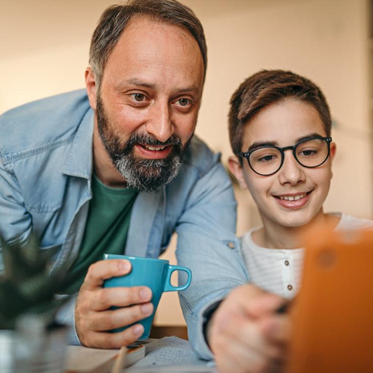A father is pointing at a tablet with his son during an online class