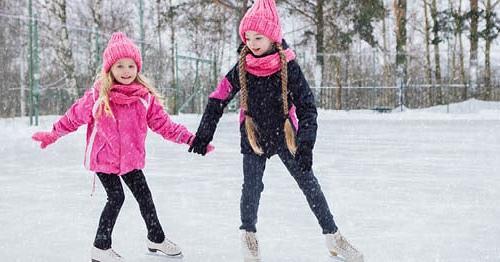 两个穿着粉色外套的年轻女性在溜冰场上滑冰，享受着下雪的冬日. 
